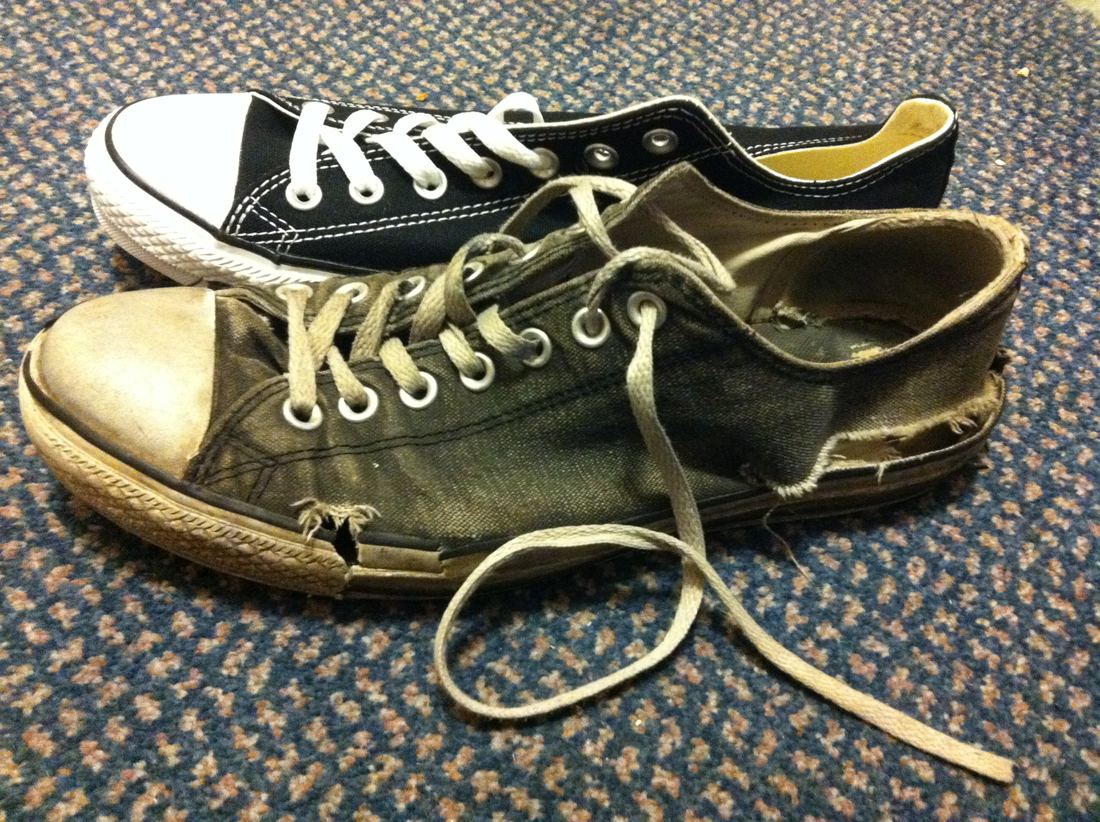 A brand new black low-top canvas sneaker beside an old one in the same style that is faded, frayed and torn along the side