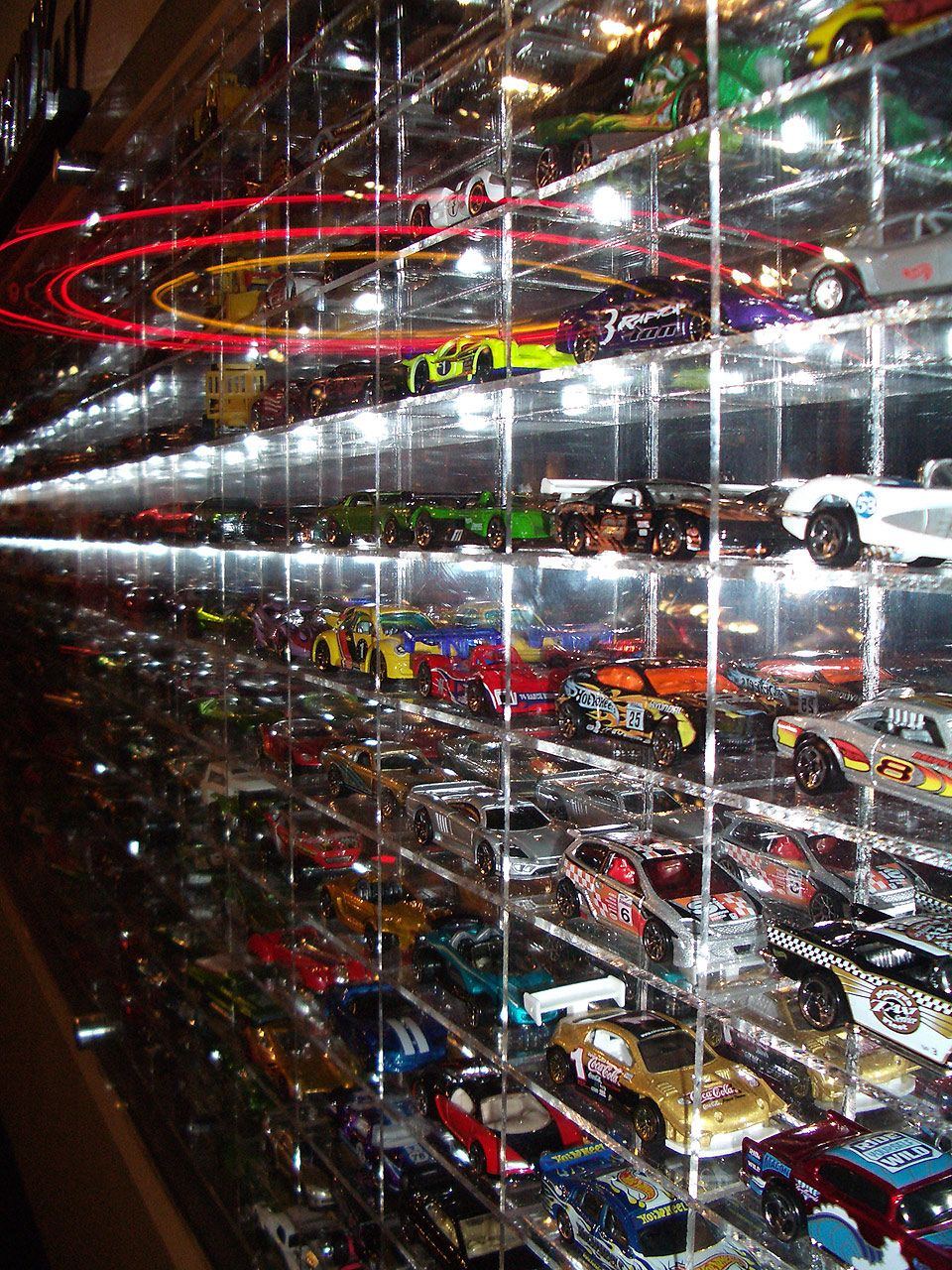 A tall clear acrylic display wall packed shelf after shelf with brightly colored die-cast toy cars